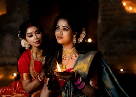 Two Indian women in sarees holding a diya, capturing the essence of elegance and tradition.